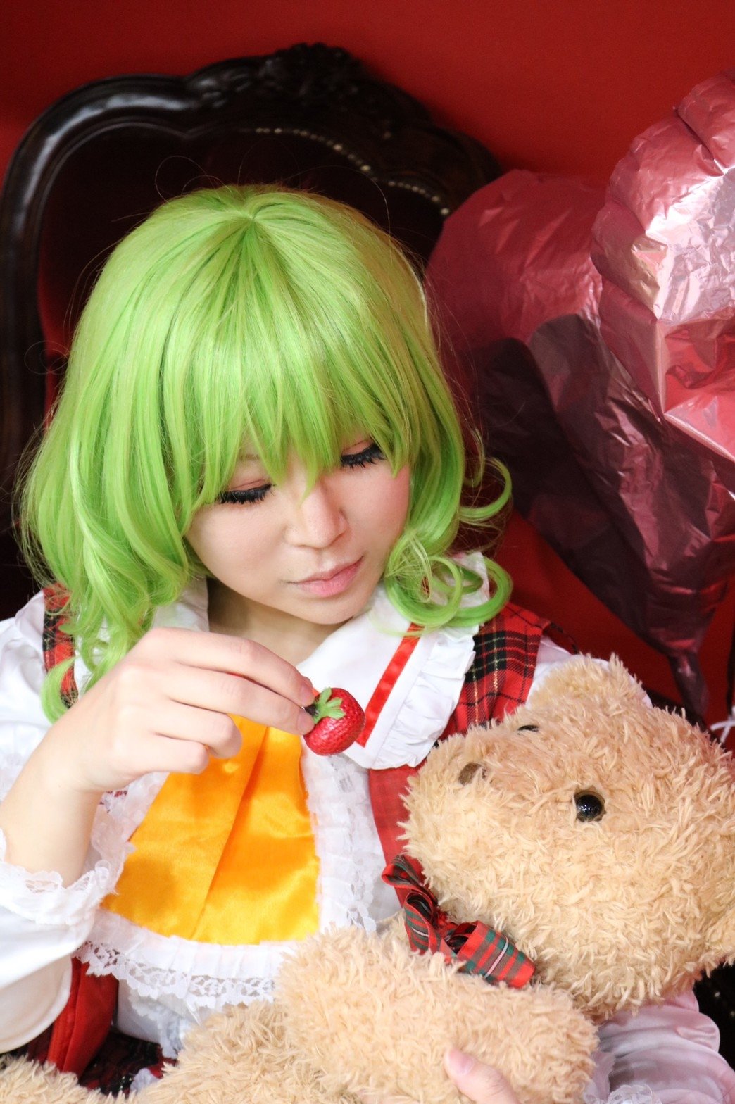 1girl ascot asian balloon bangs chair closed_eyes commentary_request cosplay eyelashes feeding food frilled_ascot frilled_shirt_collar frills fruit green_hair hair_between_eyes hand_up heart heart_balloon highres holding holding_food holding_fruit holding_stuffed_animal kazami_yuuka kazami_yuuka_(cosplay) lace_trim photo plaid plaid_vest red_vest short_hair smile solo strawberry stuffed_animal stuffed_toy teddy_bear touhou upper_body vest yellow_neckwear