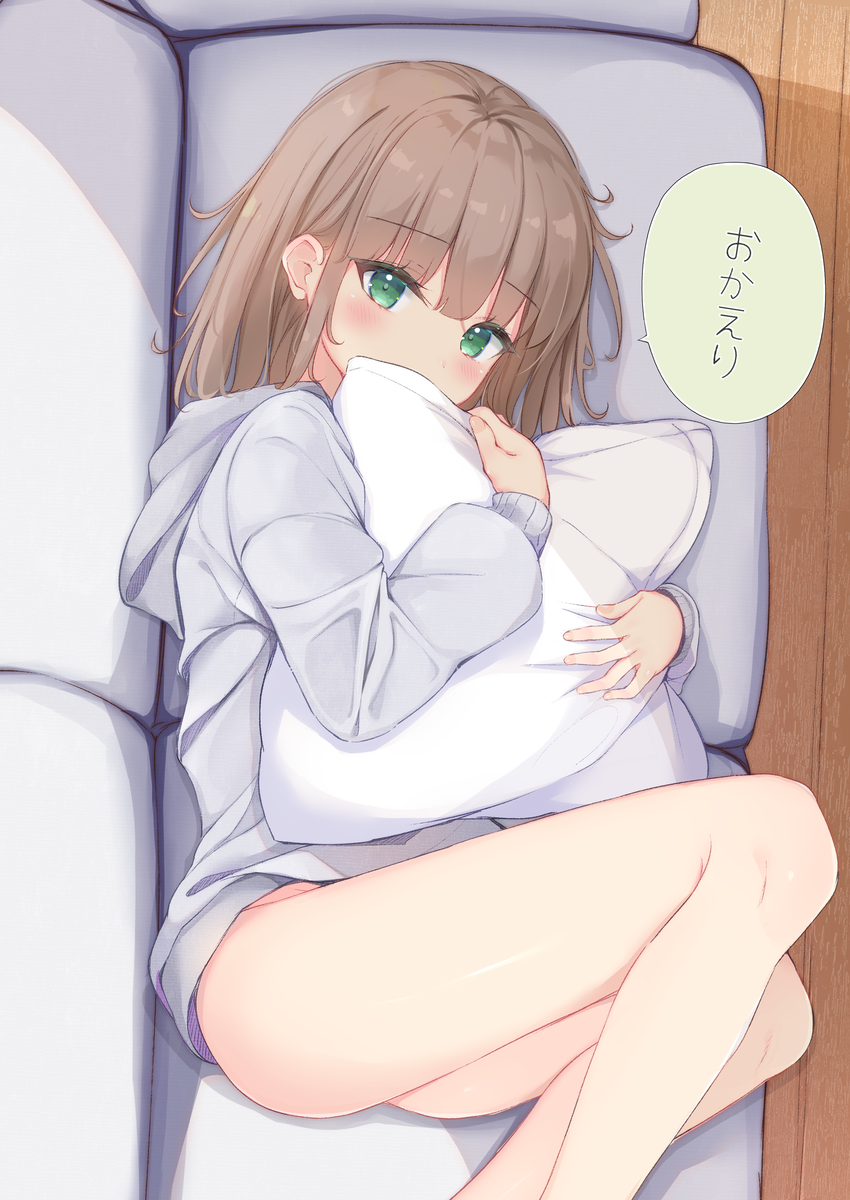 1girl bangs blush brown_hair commentary_request couch covered_mouth eyebrows_visible_through_hair feet_out_of_frame green_eyes grey_hoodie highres hood hood_down hoodie indoors long_hair long_sleeves looking_at_viewer lying on_couch on_side original pillow pillow_hug sashima solo translated wooden_floor
