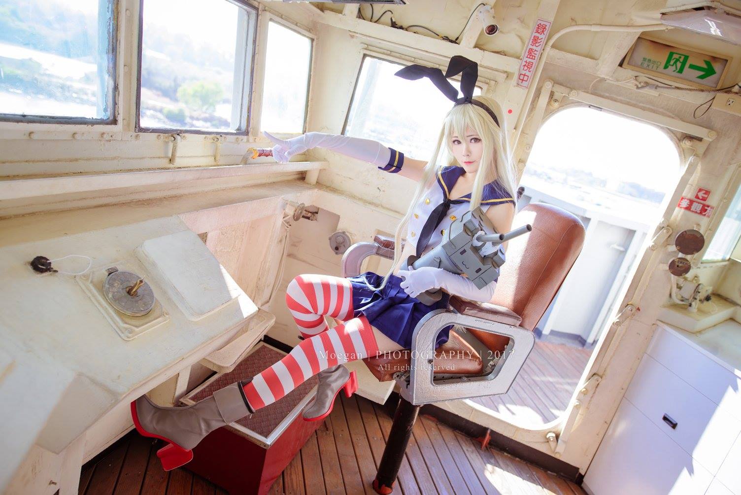1girl arty_huang_(cosplayer) blonde_hair boots brown_eyes chinese_text cosplay_photo elbow_gloves full_body gloves hairband indoors kantai_collection long_hair looking_at_viewer mismatched_eyebrows photo_(medium) pink_lips pointing rensouhou-chan school_uniform second-party_source serafuku shimakaze_(kancolle) ship sitting solo striped striped_legwear thigh-highs watercraft watermark white_gloves window