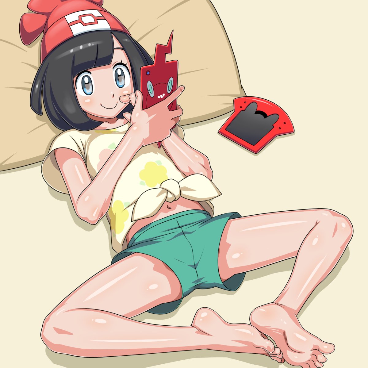 1girl bare_legs bare_midriff barefoot beanie black_eyes black_hair full_body green_shorts gun highres laying_down pillow pokemon pokemon_sm red_hat rotom_dex rotom_phone selene_(pokemon) smile soles solo tied_shirt toes white_shirt