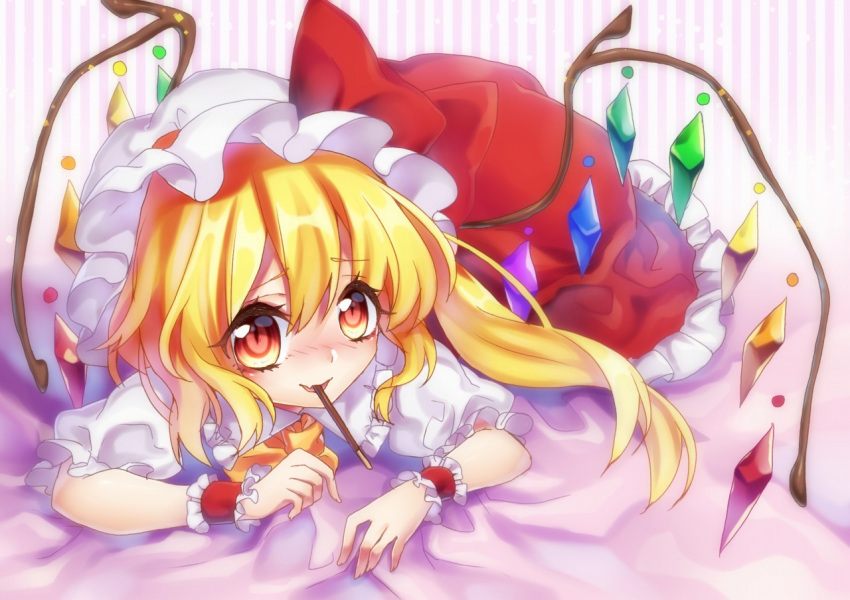1girl :d ascot bed_sheet blonde_hair blush flandre_scarlet looking_at_viewer lying mob_cap mouth_hold on_stomach open_mouth orange_eyes pocky side_ponytail smile solo suzuka_sario touhou wings wrist_cuffs