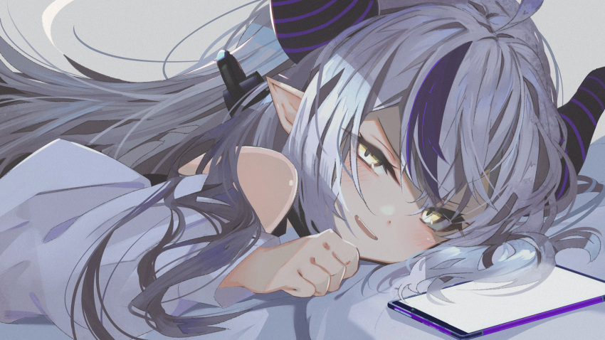 1girl :d anzi bangs bare_shoulders bed_sheet blush cellphone commentary_request demon_horns fang grey_background grey_hair hair_between_eyes half-closed_eyes hand_up highres hololive horns la+_darknesss long_hair long_sleeves looking_at_viewer lying multicolored_hair on_stomach phone purple_hair shirt simple_background smile solo streaked_hair virtual_youtuber white_shirt yellow_eyes