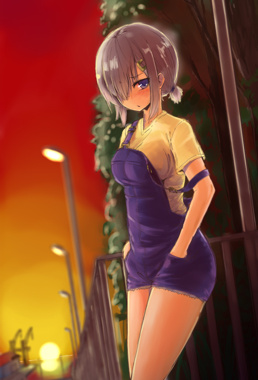 1girl alternate_costume blue_eyes blush caesar8149 cowboy_shot hair_ornament hair_over_one_eye hairclip hamakaze_(kantai_collection) highres kantai_collection looking_at_viewer overalls short_hair short_sleeves silver_hair solo strap_slip sunset t-shirt