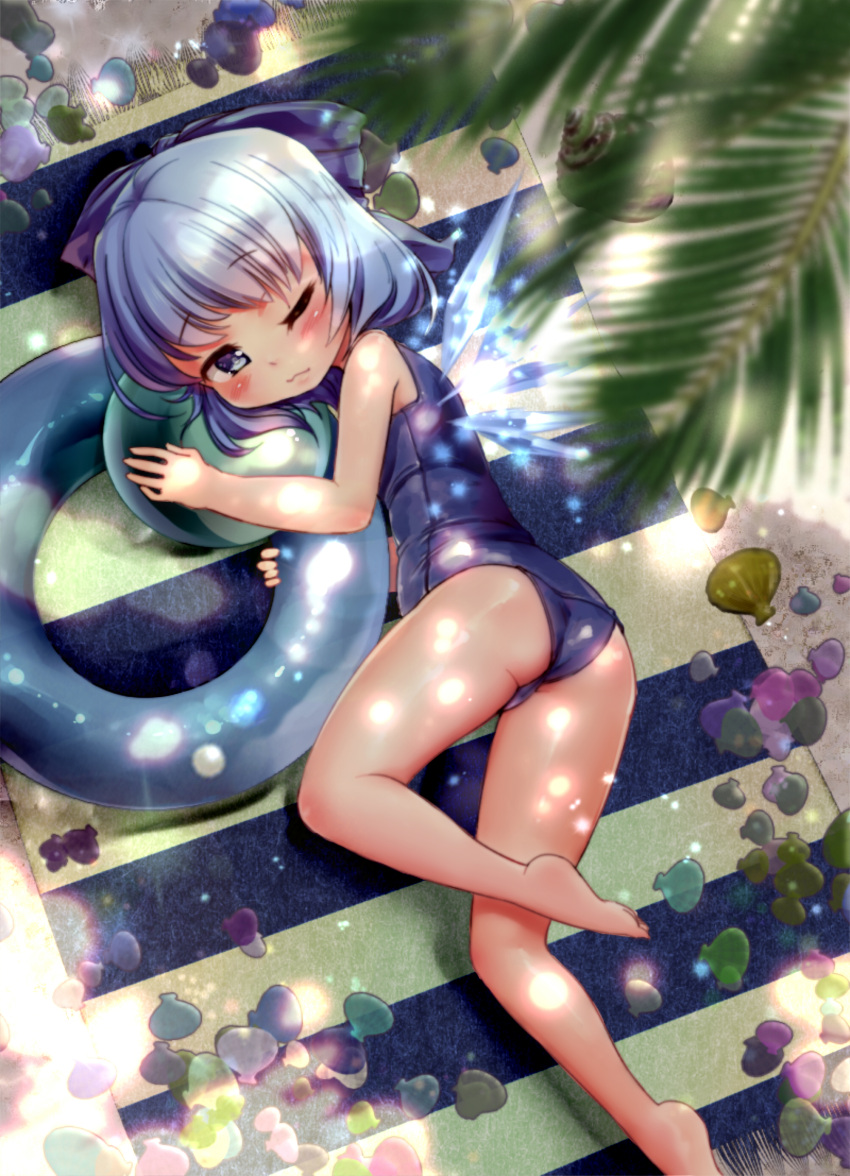 1girl absurdres ball beachball blanket blue_eyes blue_hair bow cirno dappled_sunlight hair_bow highres ice ice_wings innertube looking_at_viewer lying on_side one_eye_closed palm_tree school_swimsuit shell solo swimsuit touhou tree volcano_(liao) wings