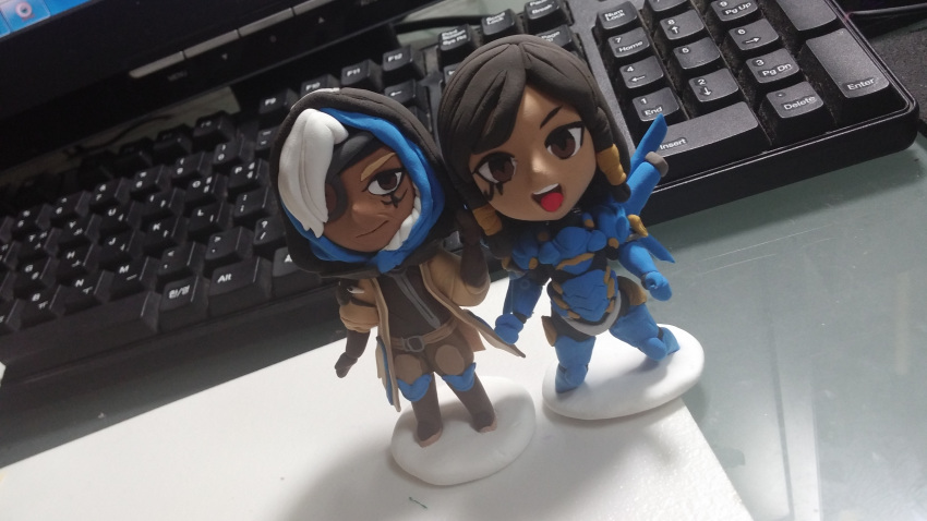 2girls :d absurdres ana_(overwatch) black_hair boots brown_boots brown_eyes brown_gloves chibi clay coat commentary computer_keyboard dark_skin desk eye_of_horus eyepatch facial_mark facial_tattoo figure flowerrain1612 full_body gloves hair_tubes highres hijab hood looking_at_viewer mother_and_daughter multiple_girls old_woman open_mouth overwatch pharah_(overwatch) photo power_armor side_braids smile standing tattoo traditional_media white_hair
