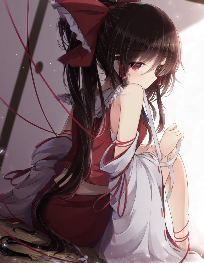 1girl black_hair bow detached_sleeves gohei hair_bow hair_tubes hakurei_reimu highres indoors long_hair looking_at_viewer ponytail red_bow red_eyes red_skirt red_string ribbon-trimmed_sleeves ribbon_trim sarashi shide sitting skirt sliding_doors solo string tatami touhou very_long_hair vest yutaka_saki_shu