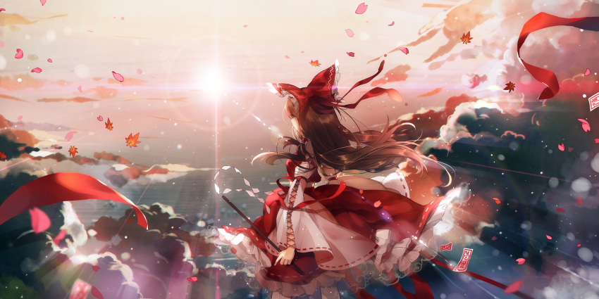 1girl bow brown_hair clouds day detached_sleeves floating_hair from_behind hair_bow hakurei_reimu highres holding leaf lens_flare long_hair long_skirt outdoors petals red_bow red_ribbon red_shirt red_skirt ribbon ribbon-trimmed_sleeves ribbon_trim rokusai shirt skirt solo standing sunlight touhou very_long_hair