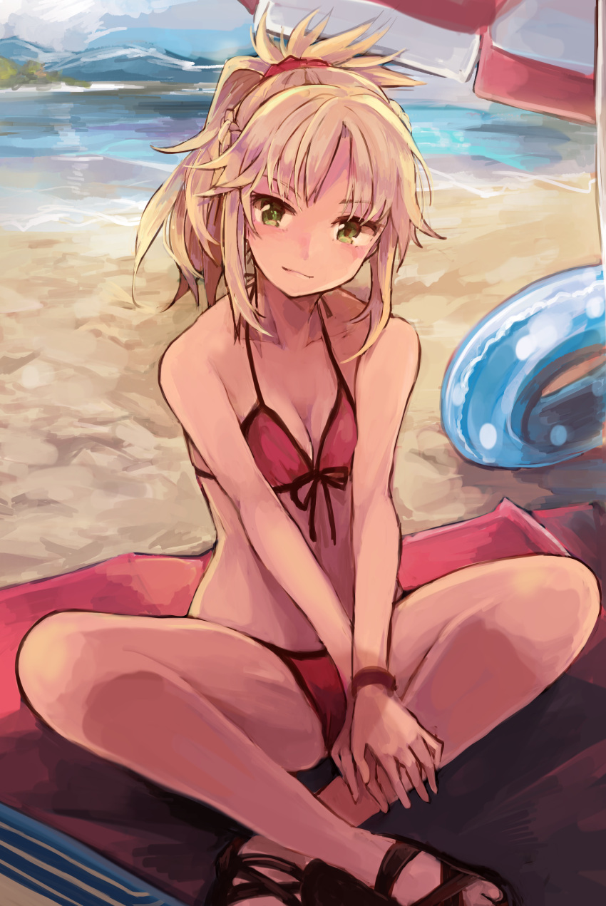 1girl absurdres beach beach_towel beach_umbrella bikini blonde_hair bracelet collarbone day fate/grand_order fate_(series) front-tie_bikini front-tie_top green_eyes hair_ornament hair_scrunchie highres indian_style innertube jewelry looking_at_viewer mitu-yuki mordred_(fate)_(all) mordred_(swimsuit_rider)_(fate) mountain ponytail red_bikini scrunchie side-tie_bikini sitting smile solo swimsuit towel umbrella v_arms water