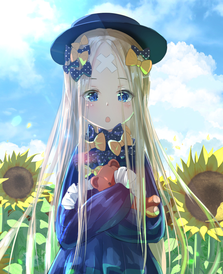 1girl abigail_williams_(fate/grand_order) bangs black_bow black_dress black_hat blonde_hair blue_eyes blue_sky blush bow crossed_bandaids dress fate/grand_order fate_(series) field flower flower_field forehead hair_bow hat highres holding holding_stuffed_animal long_hair long_sleeves looking_at_viewer object_hug open_mouth orange_bow parted_bangs polka_dot polka_dot_bow sakazakinchan sky sleeves_past_fingers sleeves_past_wrists solo stuffed_animal stuffed_toy sunflower sunlight teddy_bear