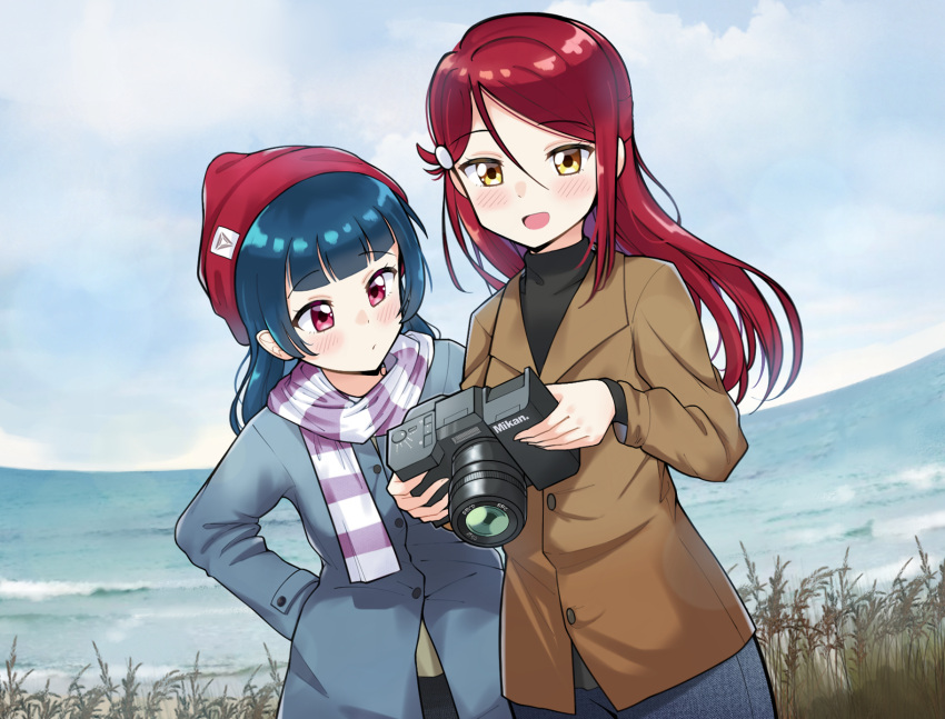 2girls :d bangs beanie black_shirt blue_coat blue_hair blunt_bangs blush brand_name_imitation brown_coat camera ceph_(greatyazawa1819) coat commentary_request day grass hair_ornament hairclip hand_on_hip hat highres holding holding_camera long_hair long_sleeves love_live! love_live!_sunshine!! multiple_girls nikon_(company) ocean open_mouth outdoors red_eyes red_hat redhead sakurauchi_riko scarf shirt smile striped striped_scarf tsushima_yoshiko winter_clothes yellow_eyes