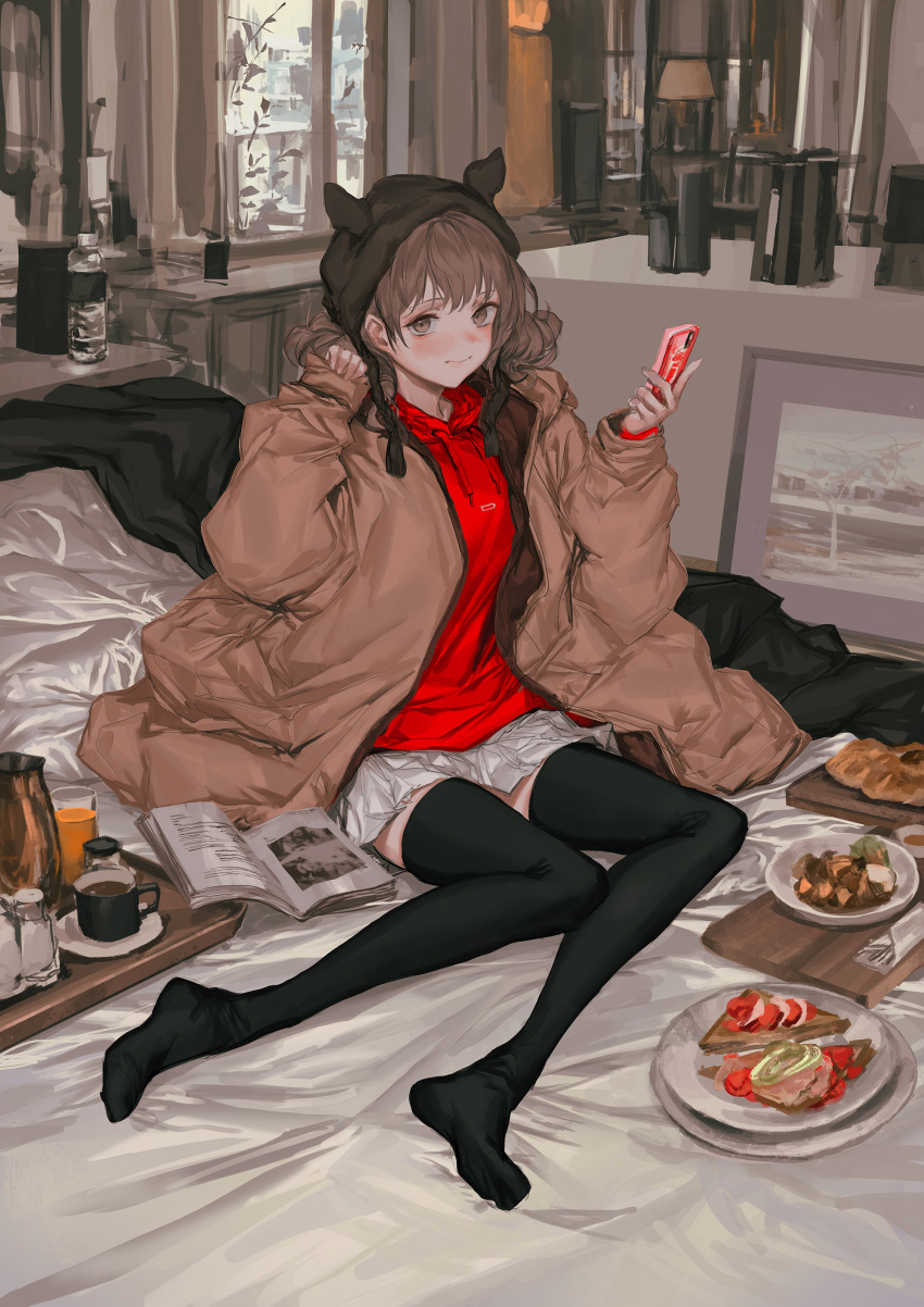 1girl absurdres apartment bangs barefoot bed bed_sheet bedroom black_legwear blanket blush brown_coat brown_eyes brown_hair cellphone cityscape coat coffee_pot counter food highres holding holding_phone indoors knit_hat lm7_(op-center) long_hair magazine on_bed open_clothes open_coat original phone picture_frame red_shirt shirt sitting sitting_on_bed skirt smile solo white_skirt window