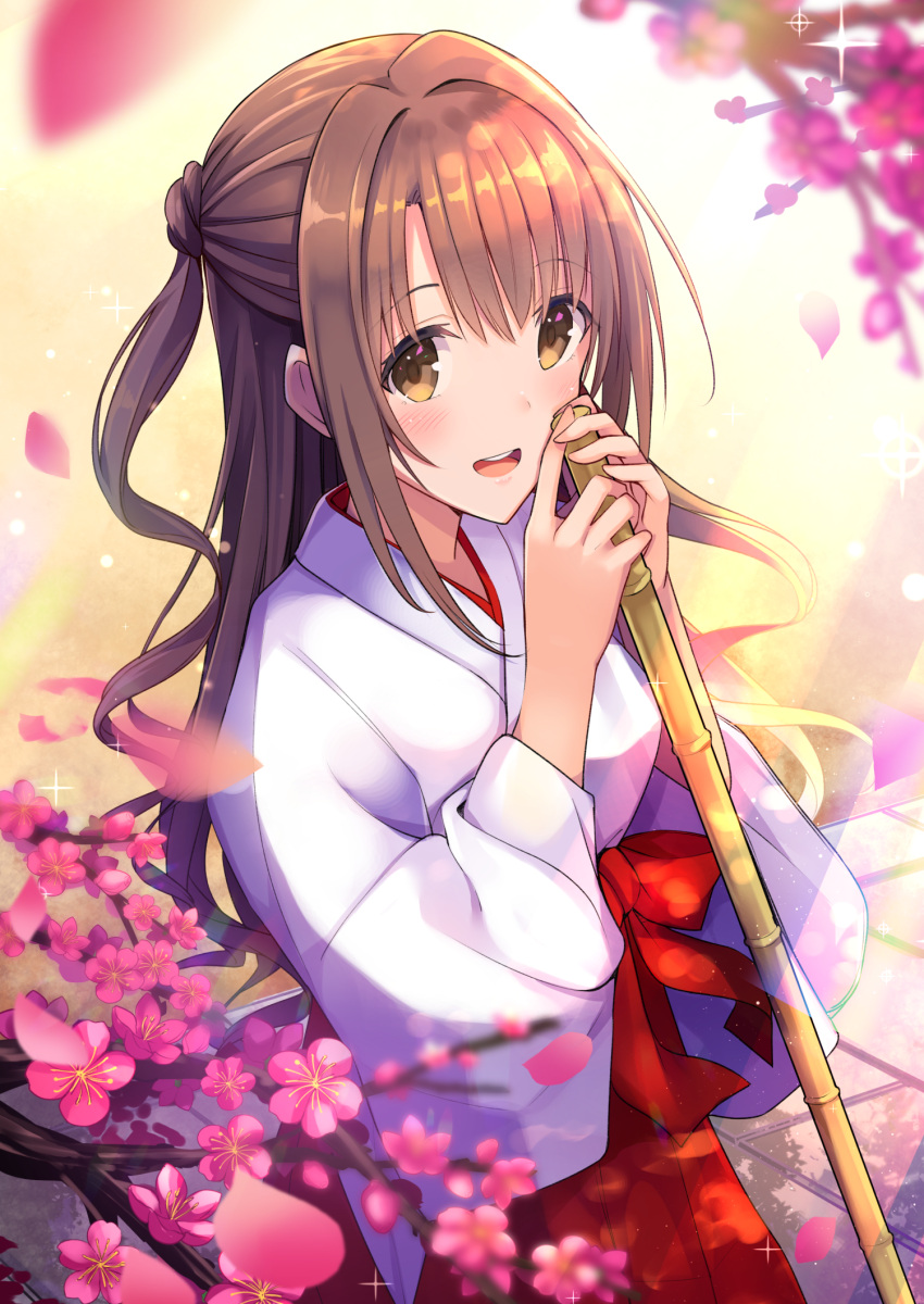 1girl :d bamboo bangs blurry blush brown_eyes brown_hair cowboy_shot depth_of_field eyebrows_visible_through_hair flower hair_intakes hakama highres holding idolmaster idolmaster_cinderella_girls japanese_clothes light_particles long_hair long_sleeves looking_at_viewer miko one_side_up open_mouth petals pink_flower red_hakama shimamura_uzuki sidelocks smile solo standing u_rin upper_teeth wavy_hair wide_sleeves