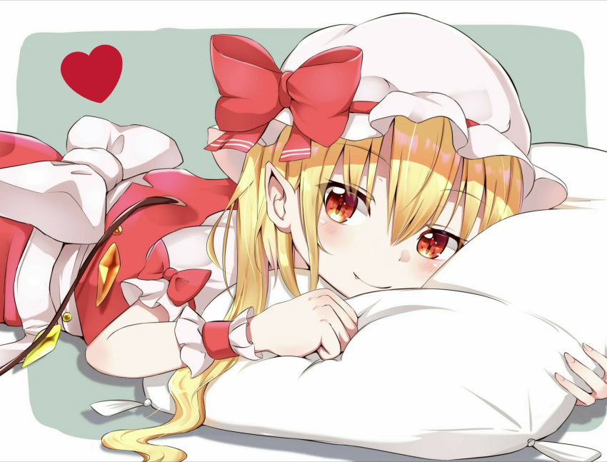 1girl blonde_hair blush clenched_hand eyebrows_visible_through_hair fang fang_out flandre_scarlet grey_background hair_between_eyes hat hat_ribbon head_on_pillow heart highres iyo_(ya_na_kanji) looking_at_viewer lying mob_cap on_stomach pillow pointy_ears red_eyes red_skirt red_vest ribbon shirt short_hair side_ponytail simple_background skirt slit_pupils smile solo touhou vest white_headwear white_shirt wrist_cuffs