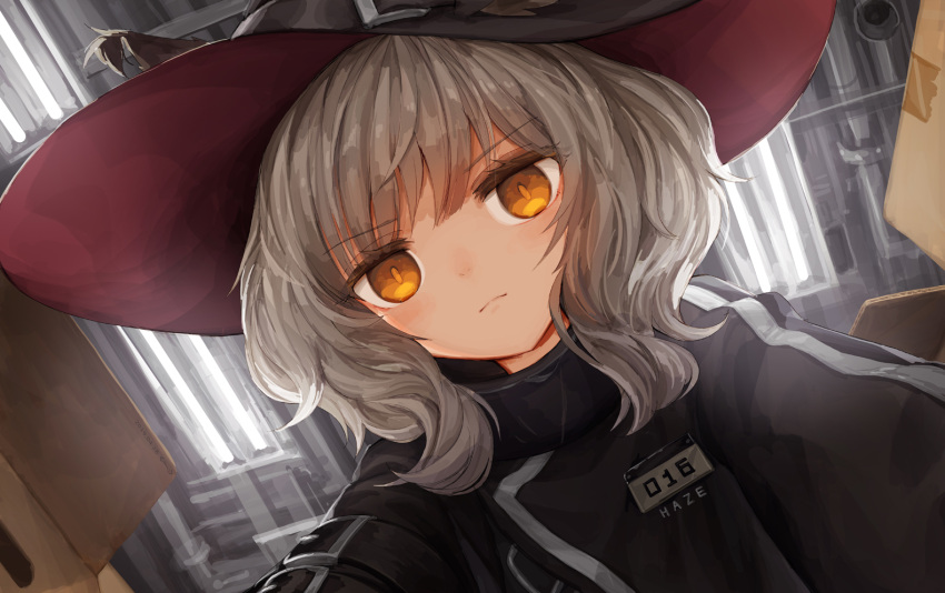 1girl arknights bangs black_headwear black_jacket box brown_eyes brown_hair cardboard_box ceiling_light closed_mouth dutch_angle eyebrows_visible_through_hair hair_between_eyes hat haze_(arknights) indoors jacket jakoujika looking_at_viewer sidelocks solo witch_hat