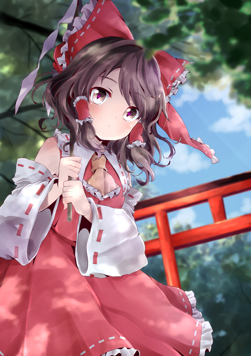 1girl ascot bangs bare_shoulders black_hair blue_sky blush bow brown_eyes clouds commentary cowboy_shot day detached_sleeves eyebrows_visible_through_hair forest frilled_ascot frilled_bow frilled_shirt_collar frills gohei hair_bow hair_tubes hakurei_reimu highres holding kuromame_(8gou) long_sleeves looking_at_viewer nature outdoors petticoat red_bow red_skirt ribbon-trimmed_bow ribbon-trimmed_collar ribbon-trimmed_skirt ribbon-trimmed_sleeves ribbon_trim short_hair sidelocks skirt skirt_set sky solo standing swept_bangs torii touhou tree wide_sleeves yellow_neckwear