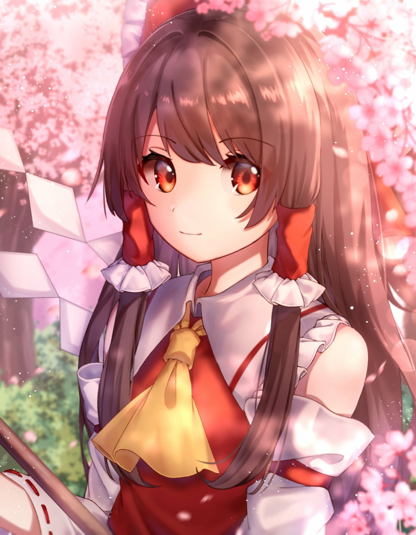 1girl bangs blurry blurry_background bow breasts brown_hair cherry_blossoms commentary cravat day depth_of_field detached_sleeves eyebrows_visible_through_hair frilled_shirt_collar frills gohei hair_bow hair_tubes hakurei_reimu highres light_smile long_hair mozuno_(mozya_7) outdoors red_eyes red_vest ribbon-trimmed_sleeves ribbon_trim sidelocks small_breasts solo standing symbol_commentary touhou tree upper_body very_long_hair vest yellow_neckwear