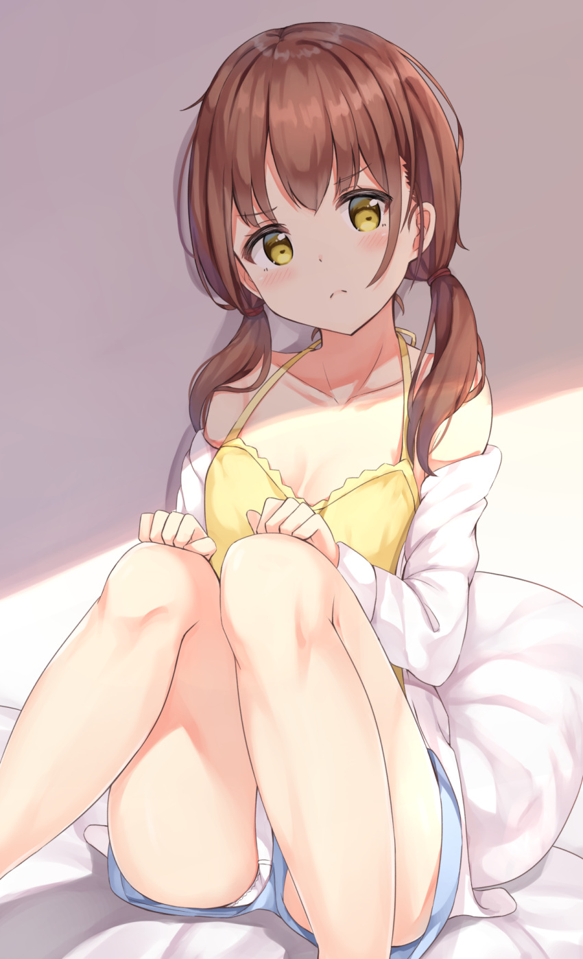 1girl blue_shorts blush brown_hair camisole collarbone feet_out_of_frame frown highres keiran_(ryo170) knees_together_feet_apart looking_at_viewer low_twintails off_shoulder original panties panties_under_shorts pantyshot pantyshot_(sitting) pillow short_shorts shorts sitting solo twintails underwear upshorts white_panties yellow_camisole yellow_eyes