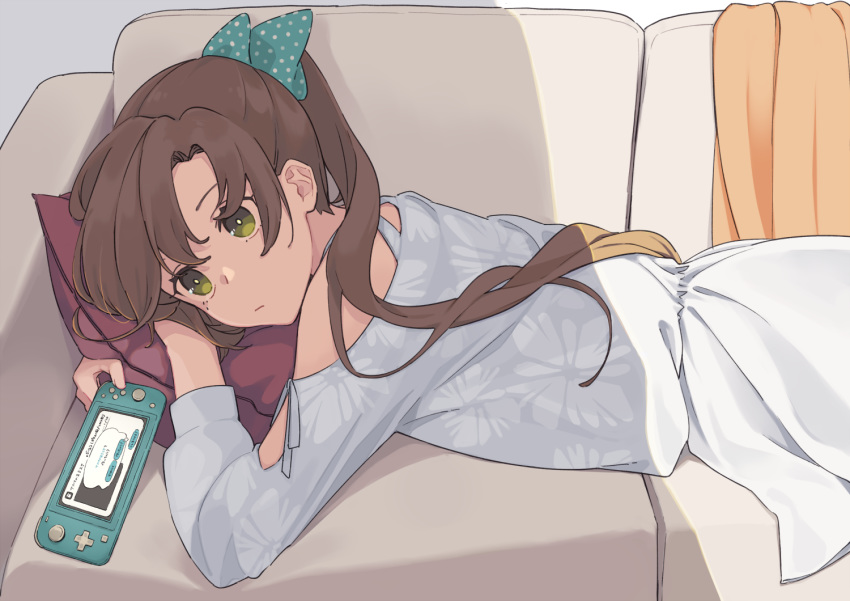 1girl akigumo_(kantai_collection) brown_hair casual commentary_request couch cowboy_shot dress green_eyes hair_ribbon handheld_game_console ichiroku_(sakumogu-029) kantai_collection long_hair lying nintendo_switch off_shoulder on_stomach polka_dot_ribbon ponytail ribbon solo white_dress