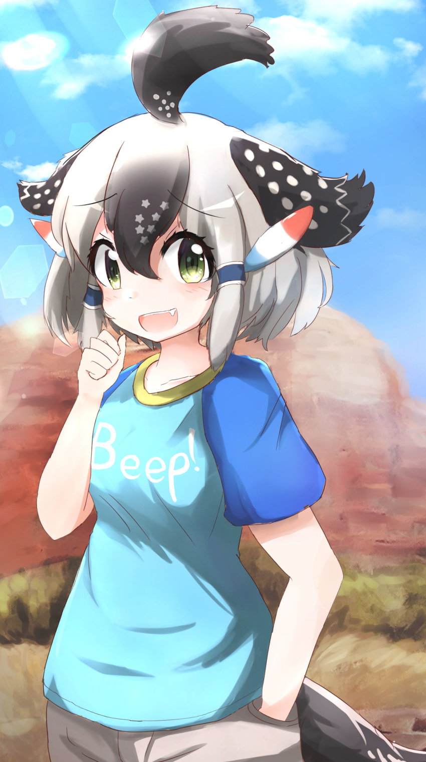 1girl ahoge arm_up bird_tail black_hair blue_shirt blue_sky blurry blurry_background clenched_hand clothes_writing clouds commentary_request day desert fang greater_roadrunner_(kemono_friends) green_eyes hand_in_pocket highres kemono_friends multicolored_hair open_mouth outdoors shirt short_sleeves shorts sky solo standing t-shirt talented_feather two-tone_hair upper_body upper_teeth white_hair