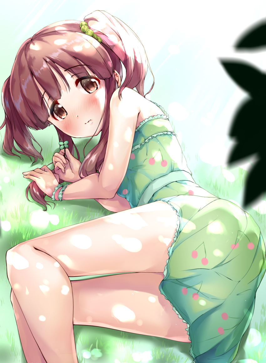 1girl ass bangs bare_shoulders blush brown_eyes brown_hair cherry_print closed_mouth clover commentary_request dress eyebrows_visible_through_hair feet_out_of_frame food_print four-leaf_clover grass green_dress green_scrunchie hair_ornament hair_scrunchie hands_up highres holding idolmaster idolmaster_cinderella_girls kuroba_aki lying ogata_chieri on_grass on_side print_dress scrunchie solo twintails wavy_mouth white_background