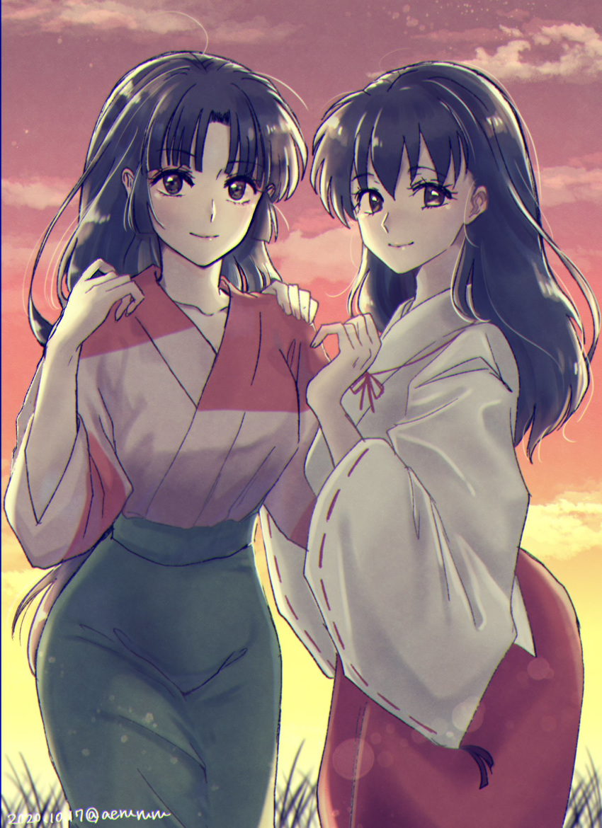 2girls aerururu bangs black_eyes black_hair blurry blush bokeh breasts closed_mouth clouds cloudy_sky commentary cowboy_shot depth_of_field eyebrows_visible_through_hair eyelashes green_skirt hand_on_another's_shoulder highres higurashi_kagome inuyasha japanese_clothes kimono lips long_hair looking_at_viewer medium_breasts miko multiple_girls outdoors parted_bangs red_skirt sango side-by-side skirt sky smile standing sunset twitter_username white_robe wide_sleeves