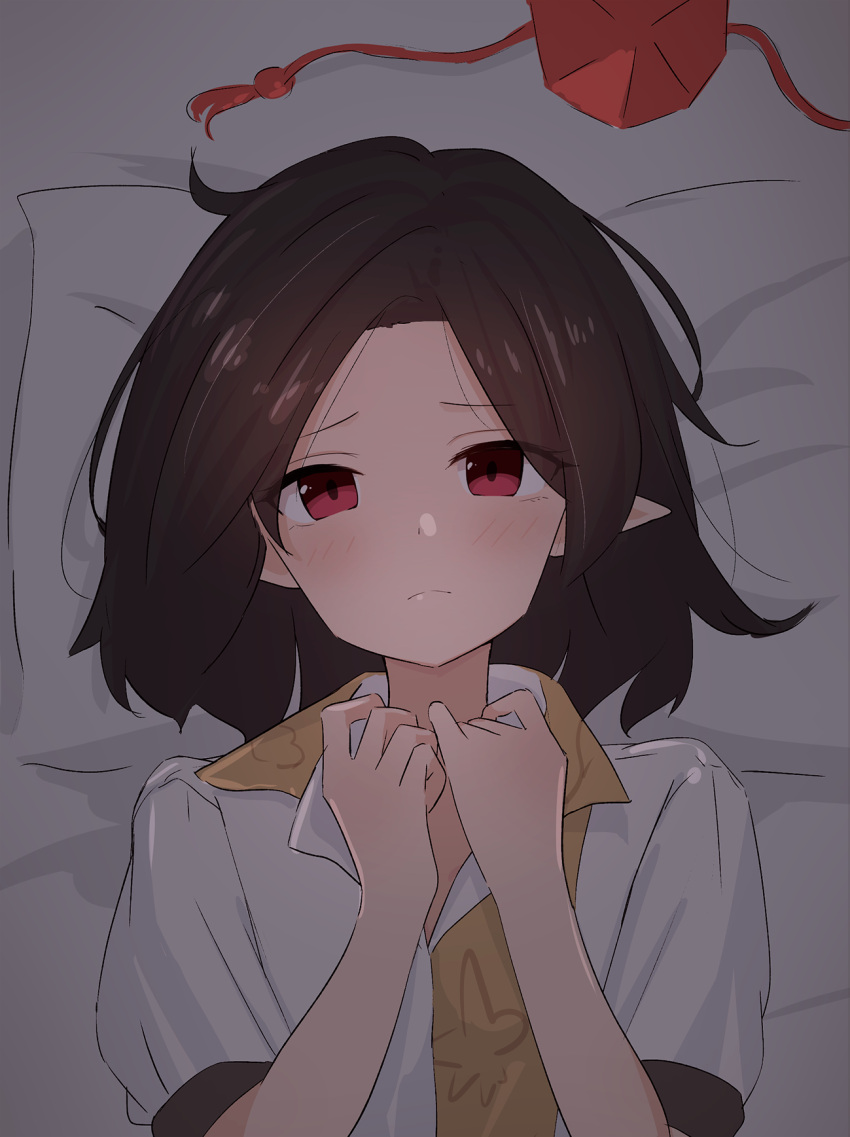 1girl black_hair blush commentary dark_room hands_on_own_chest hat hat_removed headwear_removed highres kanpa_(campagne_9) light_frown looking_at_viewer lying on_back on_bed pillow pointy_ears puffy_short_sleeves puffy_sleeves red_eyes shameimaru_aya shirt short_hair short_sleeves solo tareme tokin_hat touhou two-tone_shirt upper_body white_shirt