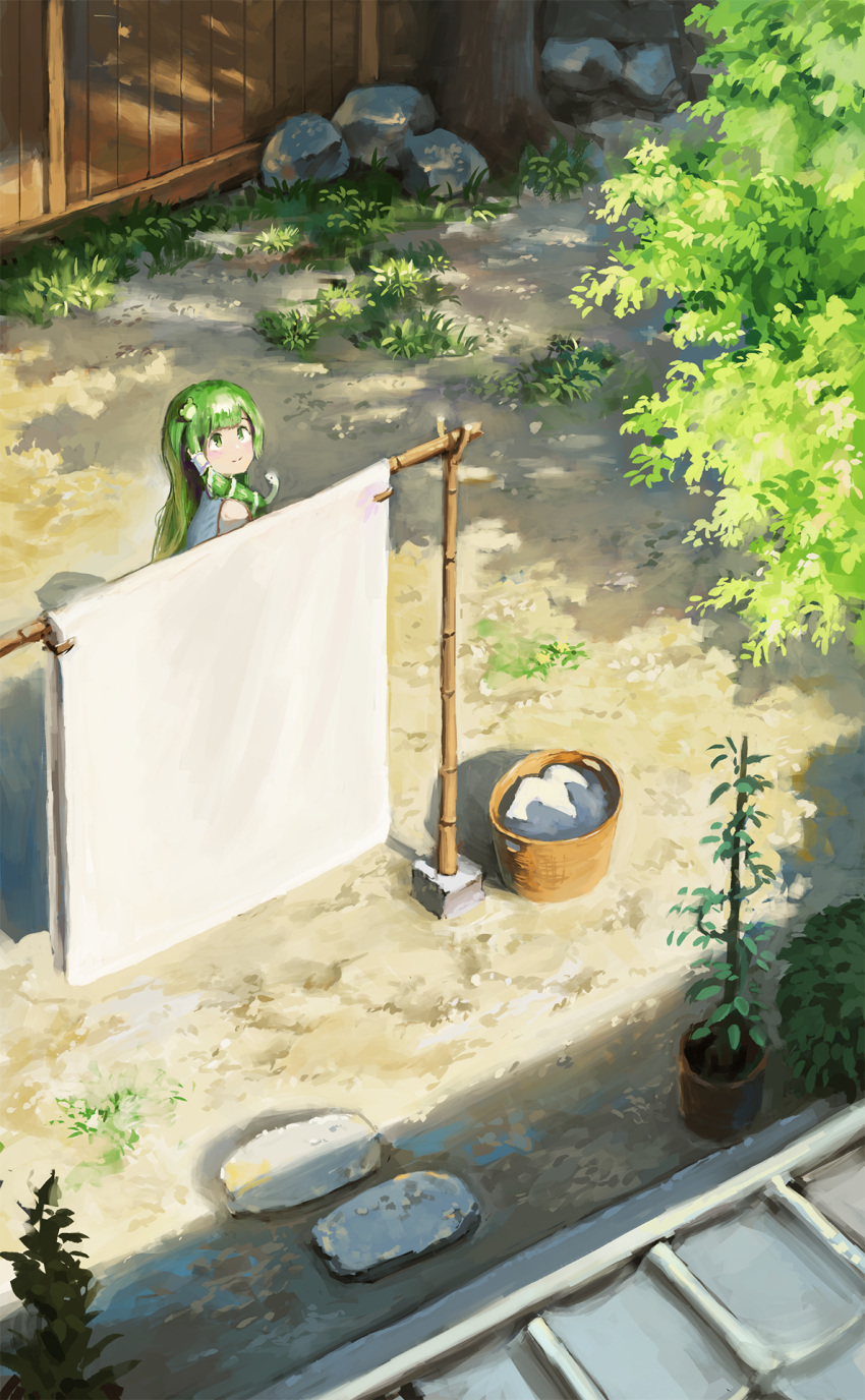 1girl alternate_eye_color alternate_hairstyle bed_sheet clothesline commentary day fjsmu frog_hair_ornament from_above grass green_eyes green_hair hair_ornament hair_tubes highres kochiya_sanae laundry_basket long_hair looking_up outdoors plant potted_plant rock shadow single_sidelock smile snake_hair_ornament solo standing stepping_stones touhou tree upper_body very_long_hair