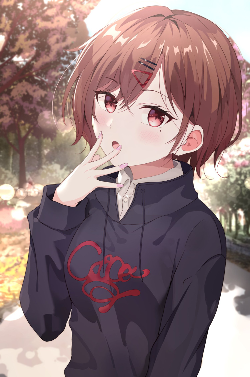 1girl brown_eyes brown_hair day eyebrows_visible_through_hair hair_ornament hairclip highres higuchi_madoka hood hoodie idolmaster idolmaster_shiny_colors long_sleeves looking_at_viewer mole mole_under_eye nail_polish open_mouth outdoors pink_nails shirt short_hair solo surrender tree