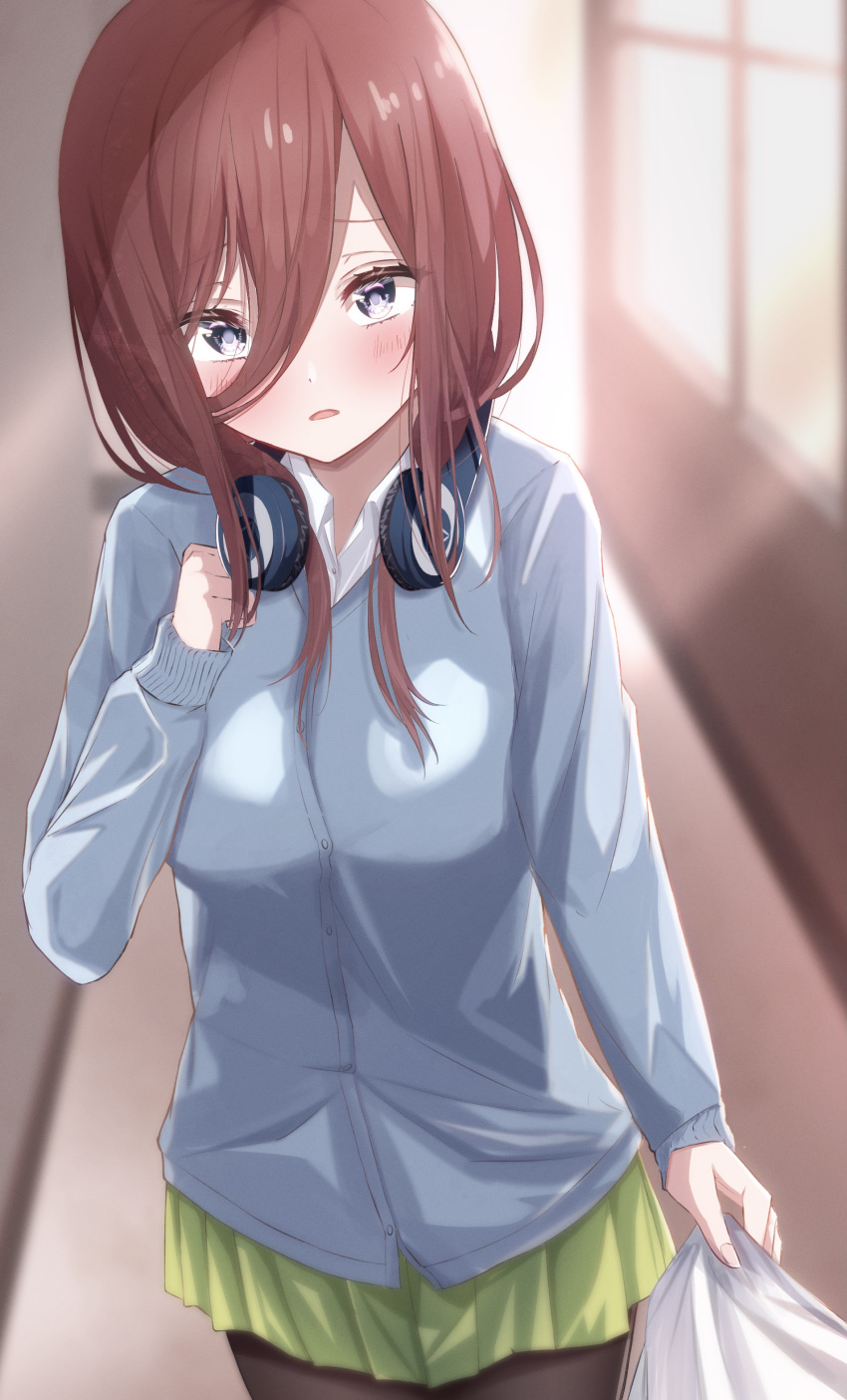 1girl absurdres bangs black_eyes blue_cardigan blurry blurry_background blush brown_hair cardigan clothes_grab commentary cowboy_shot eyebrows_behind_hair go-toubun_no_hanayome green_skirt hair_between_eyes hallway hand_up headphones headphones_around_neck highres holding indoors long_hair long_sleeves looking_at_viewer mugi nakano_miku parted_lips pleated_skirt shirt skirt solo sunlight white_shirt