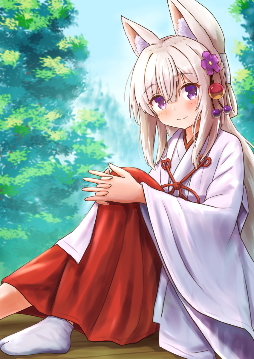 1girl absurdres animal_ear_fluff animal_ears ankle_socks bangs blush closed_mouth commentary_request day eyebrows_visible_through_hair flower folded_ponytail fox_ears hair_between_eyes hair_flower hair_ornament hakama hakama_skirt highres interlocked_fingers iroha_(iroha_matsurika) japanese_clothes kimono knee_up koyoi_(iroha_(iroha_matsurika)) light_brown_hair long_hair long_sleeves looking_at_viewer miko original outdoors purple_flower red_hakama skirt smile solo tabi tree very_long_hair violet_eyes white_kimono white_legwear wide_sleeves