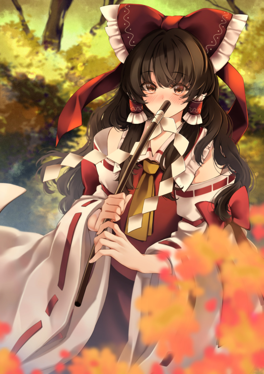 1girl ascot autumn_leaves blurry blurry_background blush bow brown_eyes brown_hair covering_mouth eyebrows_visible_through_hair frilled_shirt_collar frills gohei hair_between_eyes hair_bow hair_tubes hakurei_reimu highres long_hair looking_at_viewer meji_aniki nontraditional_miko red_bow red_skirt red_vest ribbon-trimmed_sleeves ribbon_trim skirt solo touhou vest wide_sleeves