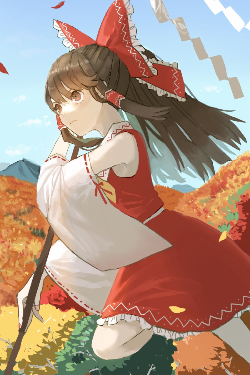 1girl arm_up ascot autumn_leaves bangs bare_shoulders belt blue_sky bow brown_eyes brown_hair closed_mouth clouds collar collared_dress detached_sleeves dress eyebrows_visible_through_hair flying frilled_bow frilled_collar frilled_dress frills gohei hair_between_eyes hair_ornament hair_tubes hakurei_reimu hand_up highres leaf leg_up long_hair long_sleeves looking_to_the_side mountain nanasuou pink_nails red_bow red_dress sky solo touhou tree white_belt wide_sleeves yellow_neckwear