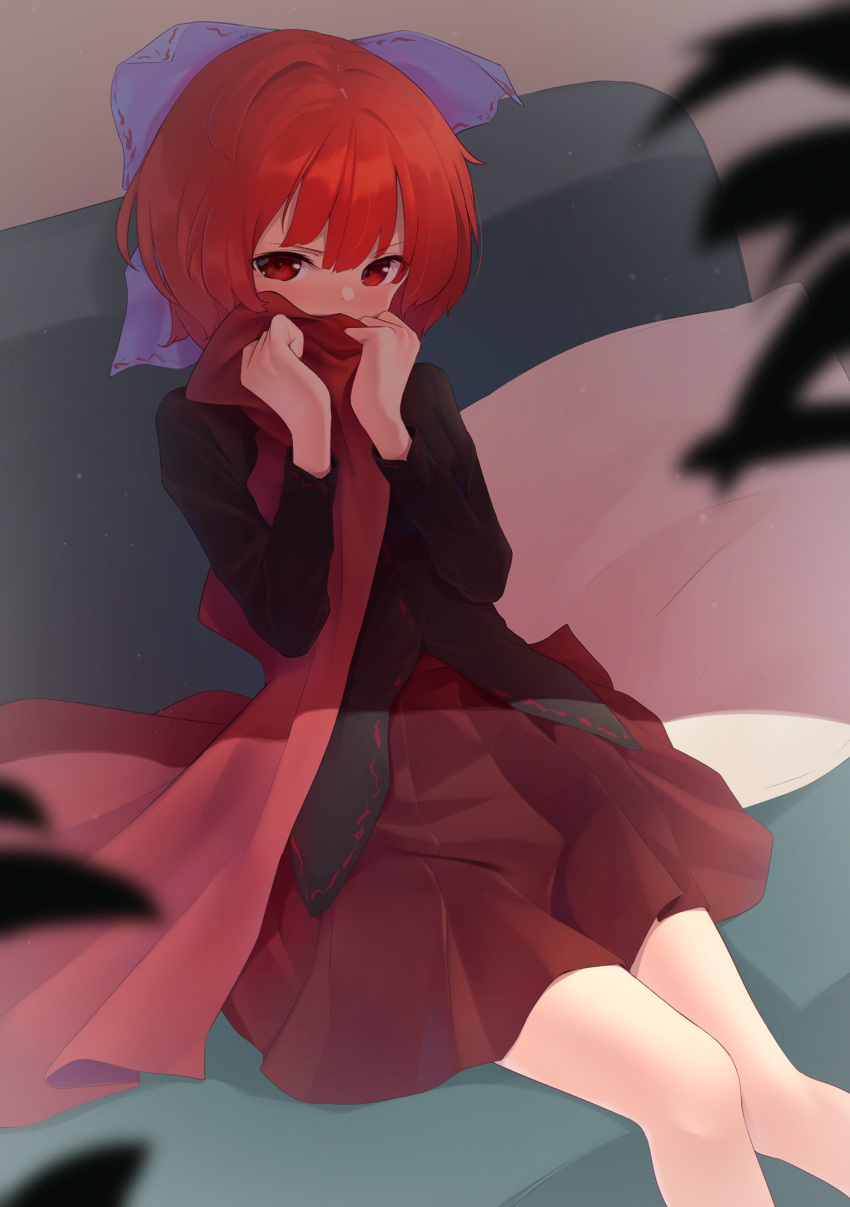 1girl bangs black_shirt blue_bow blurry blurry_foreground blush bow brown_shirt cloak couch covered_mouth covering_mouth feet_out_of_frame hair_between_eyes hair_bow hands_up highres holding holding_clothes indoors kanpa_(campagne_9) knees_together_feet_apart long_sleeves pillow pleated_skirt red_cloak red_eyes red_skirt redhead sekibanki shadow shirt short_hair sitting skirt solo touhou