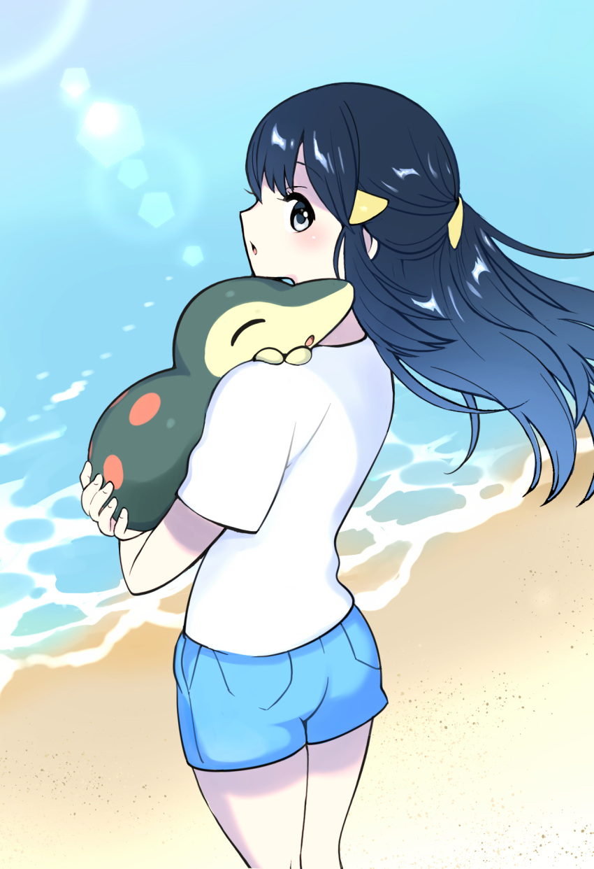 1girl akari_(pokemon) beach black_hair cyndaquil hair_ornament hairclip highres holding holding_pokemon kaniku_(pixiv5660) light_rays long_hair looking_at_viewer looking_back pokemon pokemon_(creature) pokemon_(game) pokemon_legends:_arceus short_shorts shorts standing sunlight water