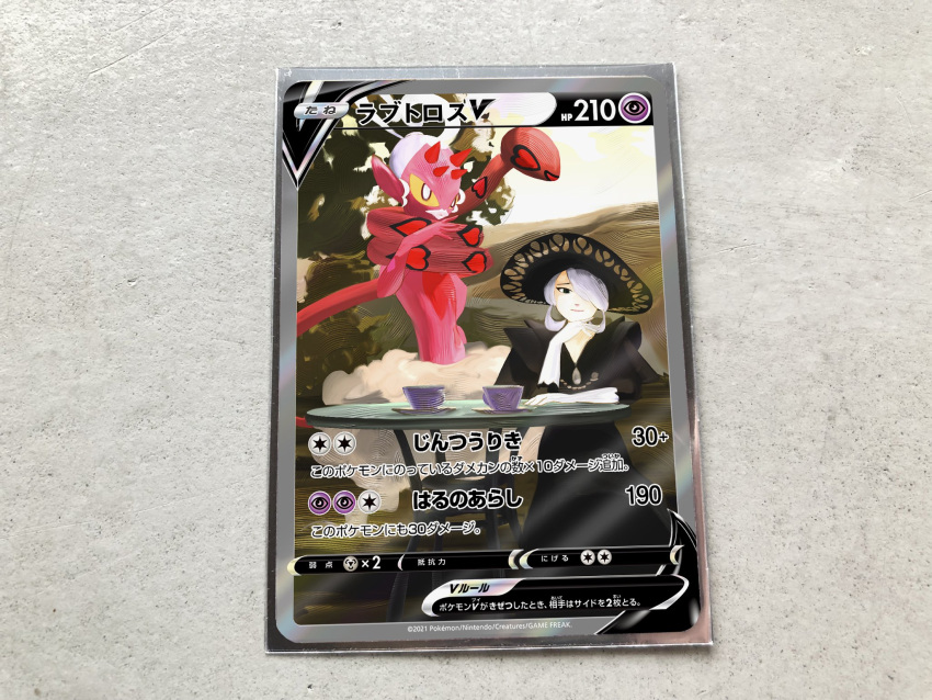 1girl black_dress black_eyes black_headwear card card_(medium) character_name character_print closed_mouth cogita_(pokemon) commentary_request cup dress enamorus_(incarnate) gloves grey_hair hair_over_one_eye hand_up hat head_rest highres looking_at_viewer official_style pokemon pokemon_(game) pokemon_legends:_arceus pokemon_tcg pokeyugami saucer short_hair smile table teacup white_gloves