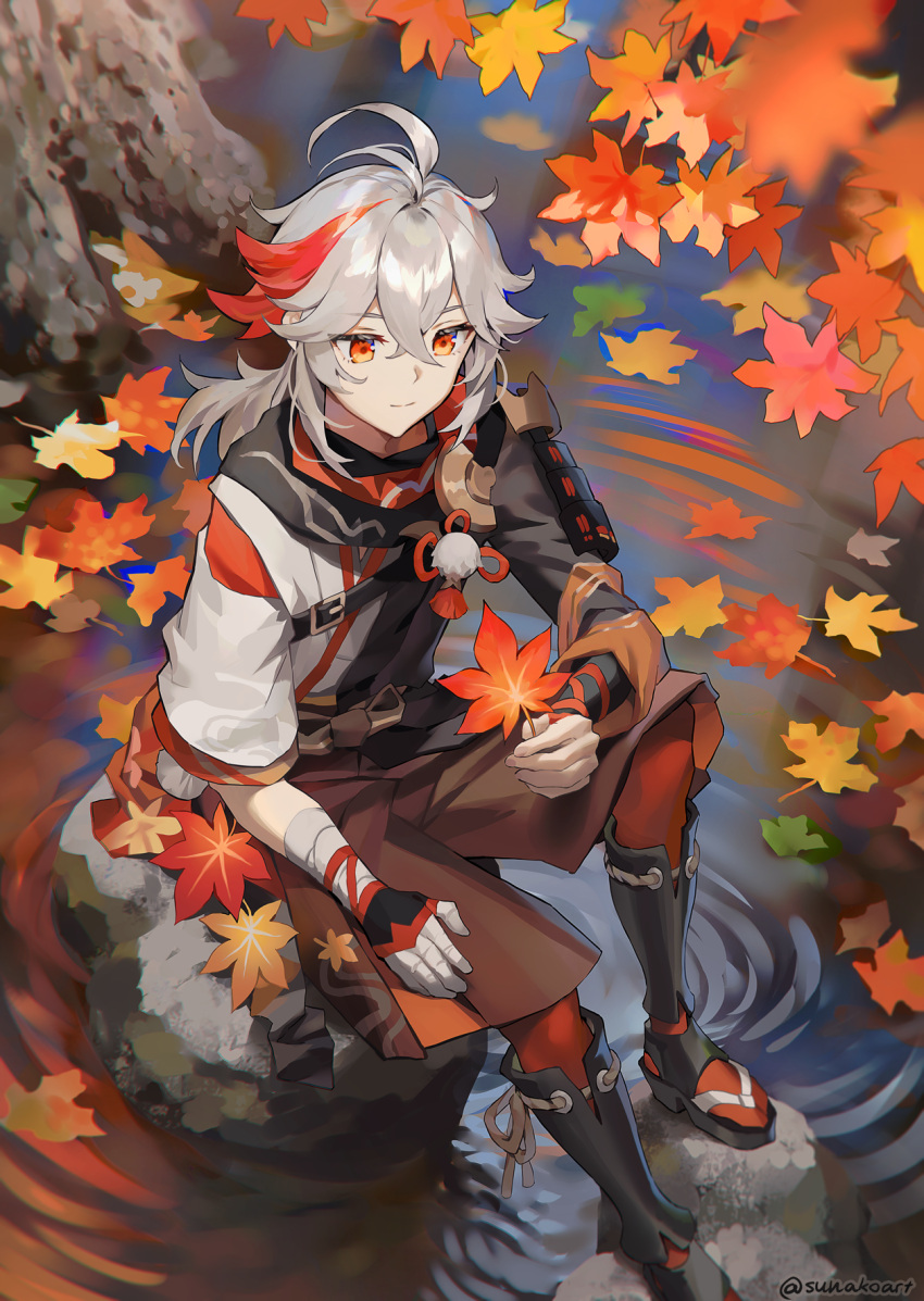 1boy autumn_leaves bangs black_footwear blurry blurry_foreground brown_shorts closed_mouth commentary day depth_of_field english_commentary genshin_impact grey_hair hair_between_eyes highres holding holding_leaf kaedehara_kazuha knee_up leaf male_focus maple_leaf multicolored_hair outdoors red_eyes redhead ripples rock short_sleeves shorts sitting smile solo streaked_hair sunako_(veera) twitter_username water