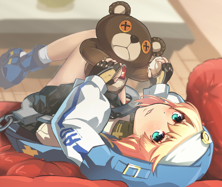 1girl androgyne_symbol aqua_eyes bike_shorts black_gloves blonde_hair blue_footwear blush bridget_(guilty_gear) couch cuffs fingerless_gloves gloves guilty_gear guilty_gear_strive habit hair_between_eyes handcuffs highres hood hoodie indoors long_sleeves looking_back medium_hair parted_lips pleated_skirt roger_(guilty_gear) shorts sitting skirt stuffed_animal stuffed_toy table teddy_bear transgender twodolls wooden_floor