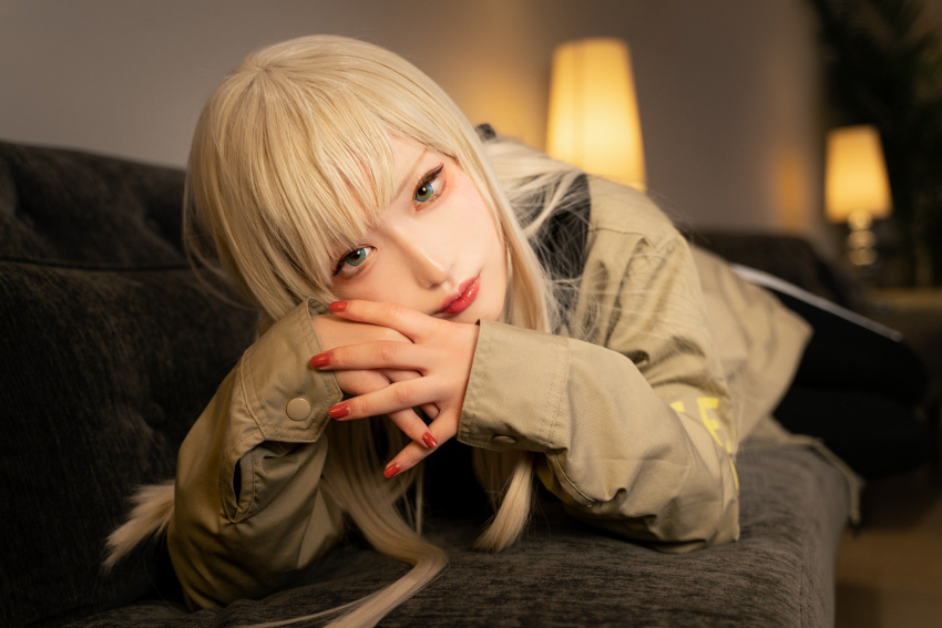 1girl bangs black_pants blonde_hair blue_eyes blurry blurry_background brown_jacket cosplay cosplay_photo couch gigi_andalusia gundam gundam_hathaway's_flash highres hisage jacket lamp long_hair looking_at_viewer lying nail_polish on_couch pants photo_(medium) red_nails solo