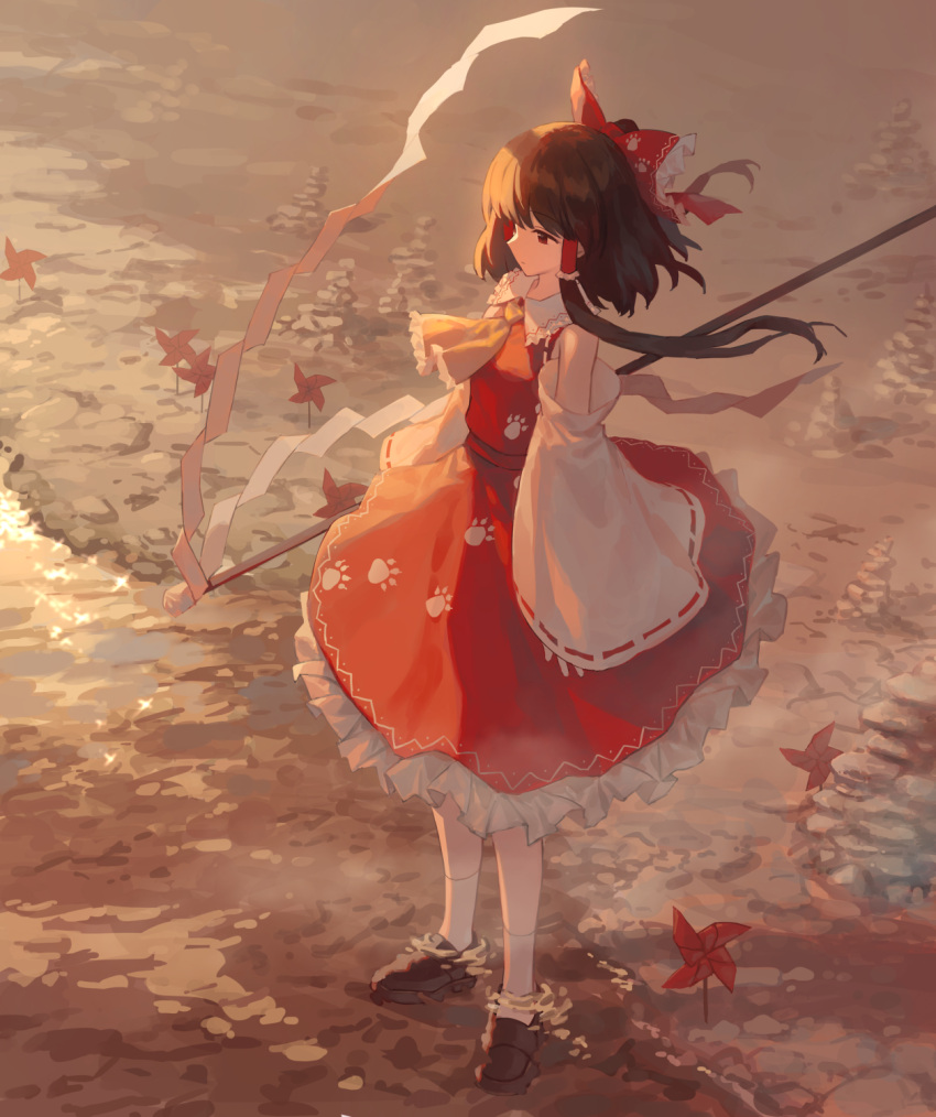 1girl ascot bad_link bangs bare_shoulders bow brown_footwear brown_hair chorefuji closed_mouth commentary_request day detached_sleeves dress floating_hair frills full_body hair_bow hair_tubes hakurei_reimu highres long_hair outdoors paw_print paw_print_pattern pinwheel red_bow red_dress shoes sidelocks sleeveless sleeveless_dress socks solo standing touhou water white_socks wide_sleeves