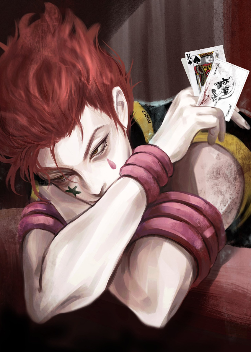 1boy card commentary_request facepaint highres hisoka_morow holding holding_card hunter_x_hunter joker_(card) king_(playing_card) korean_commentary leaning_on_object male_focus nwocp playing_card redhead short_hair sitting solo table upper_body yellow_eyes