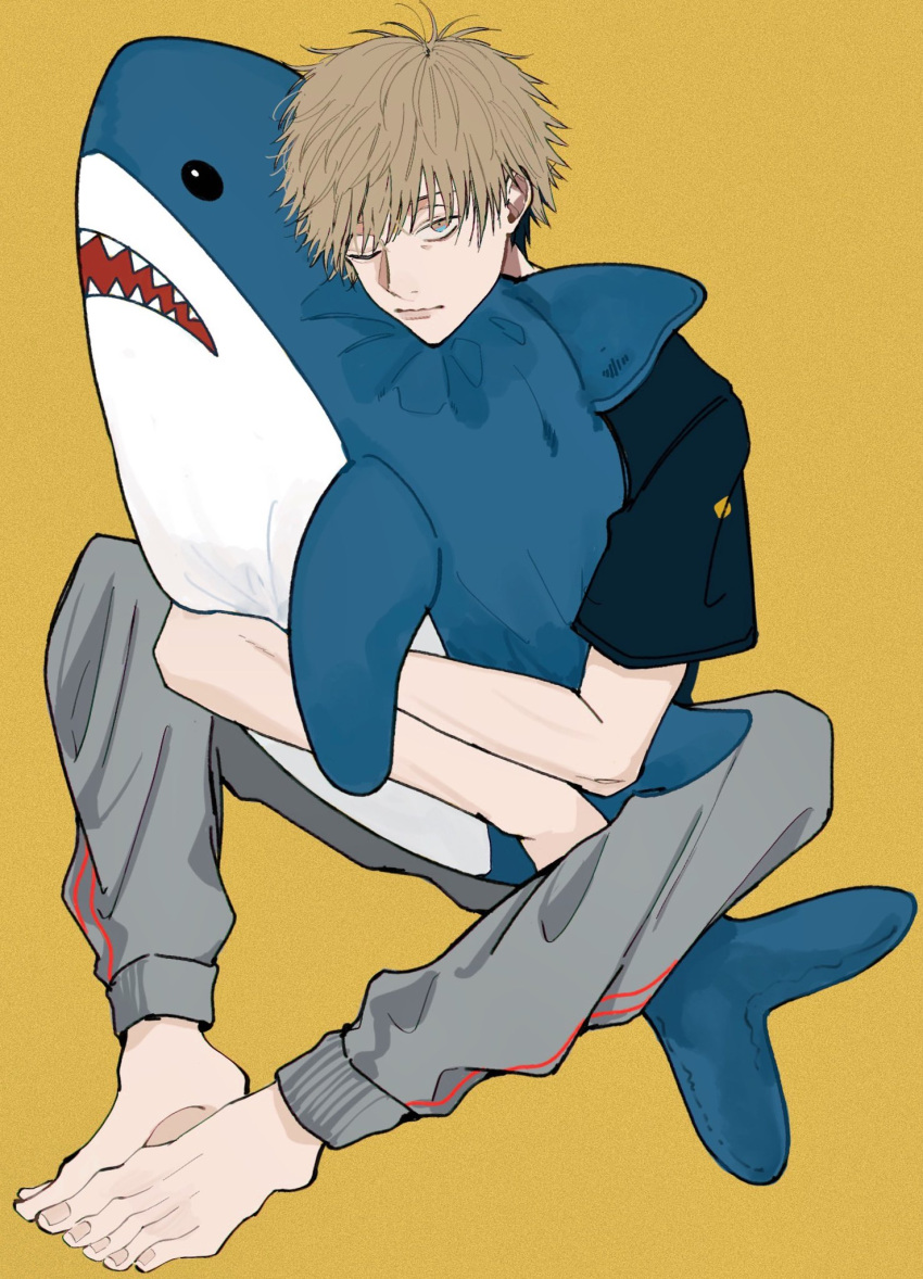 1boy barefoot blonde_hair chainsaw_man denji_(chainsaw_man) doll_hug grey_pants highres looking_at_viewer namida_a2 object_hug one_eye_closed pants shark short_hair simple_background solo track_pants yellow_background