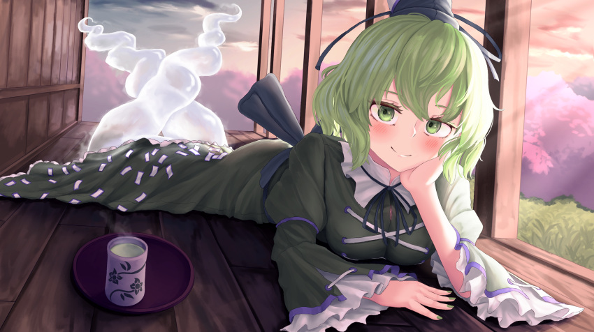 1girl black_headwear blush closed_mouth commentary cross-laced_clothes cup dress full_body ghost_tail green_dress green_eyes green_hair hand_on_own_face hat highres light_rays long_sleeves looking_at_viewer lying ofuda ofuda_on_clothes on_stomach pygrenix short_hair smile soga_no_tojiko solo tate_eboshi touhou wide_sleeves