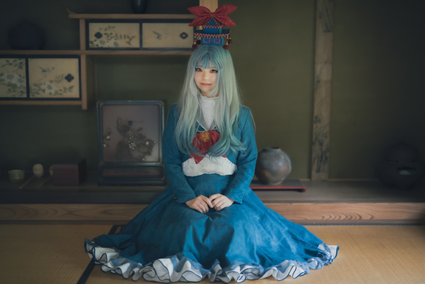 1girl absurdres architecture blue_dress blue_hair blue_headwear brown_eyes closed_mouth cosplay_photo dress east_asian_architecture frilled_dress frills full_body grey_hair hat hat_tassel highres indoors japanese_clothes kamishirasawa_keine light_smile long_sleeves looking_at_viewer multicolored_hair nasubi_iiiii own_hands_together photo_(medium) red_tassel sitting solo tatami tokin_hat touhou two-tone_hair