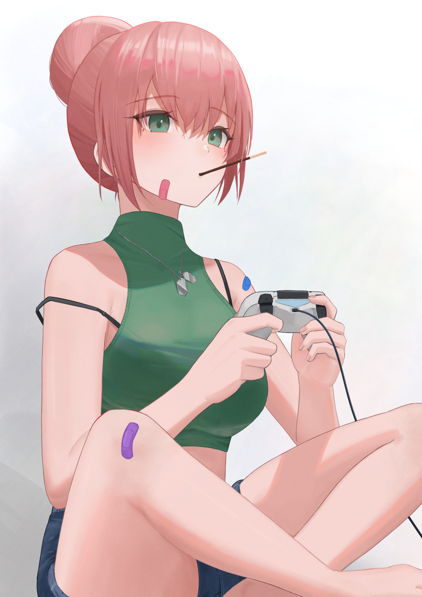 1girl absurdres bandaid bandaid_on_face bandaid_on_leg bandaid_on_shoulder bare_shoulders blue_shorts blush bra_strap breasts commentary_request controller crop_top food food_in_mouth game_controller green_eyes hair_bun highres holding holding_controller holding_game_controller indian_style jewelry long_hair necklace original pige_pig pink_hair pocky pocky_in_mouth shorts sitting solo strap_slip