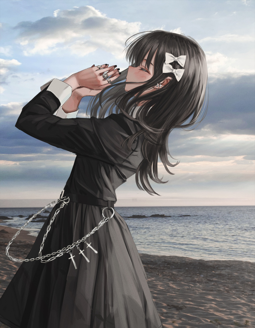1girl absurdres beach belt black_belt black_hair black_nails black_shirt black_skirt bow chain closed_eyes closed_mouth clouds cloudy_sky cowboy_shot cross day ear_piercing from_side gothic hair_bow hands_up highres jewelry latin_cross light_blush long_hair long_sleeves multiple_rings nadegata nail_polish ocean original outdoors own_hands_together photo_background piercing ring shirt skirt sky sleeve_cuffs solo standing white_bow