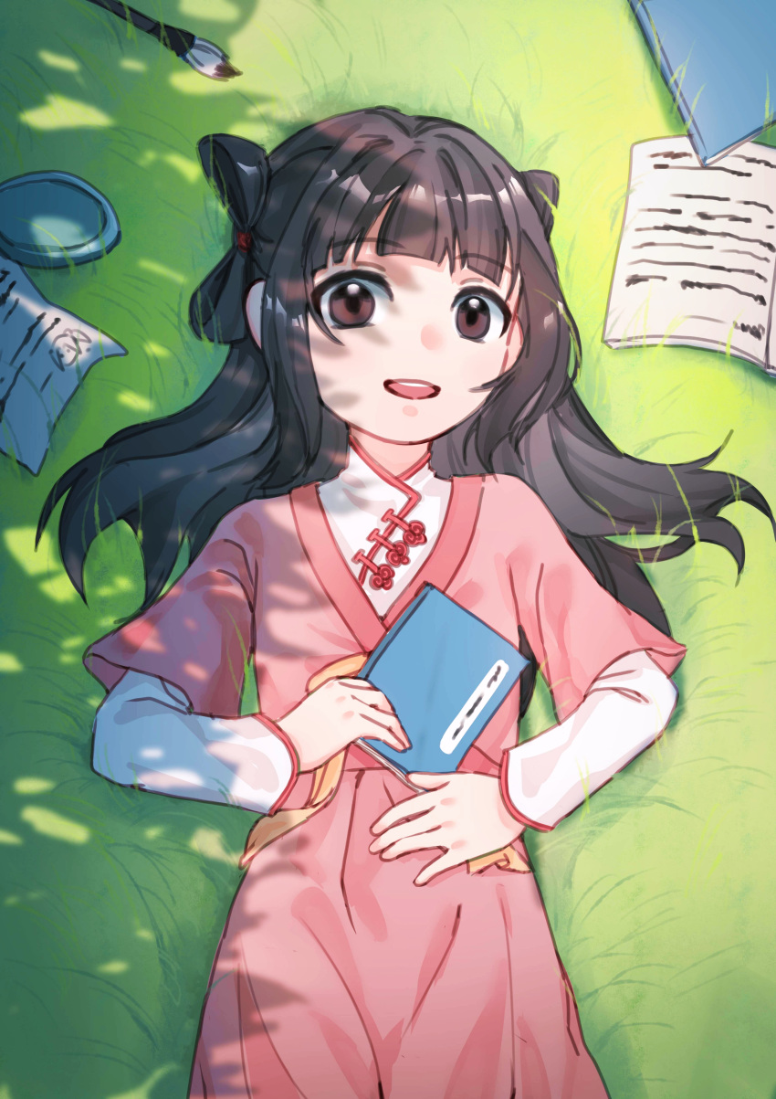 1girl :d absurdres black_hair blunt_bangs book brown_eyes chinese_clothes day dress grass hand_on_own_stomach hanfu highres holding jiang_an_an(up_in_the_heaven) jiaoling_ruqun layered_sleeves long_hair long_sleeves looking_at_viewer lying on_back on_ground open_book open_mouth outdoors paintbrush paper pink_dress short_sleeves shuangyaji smile solo