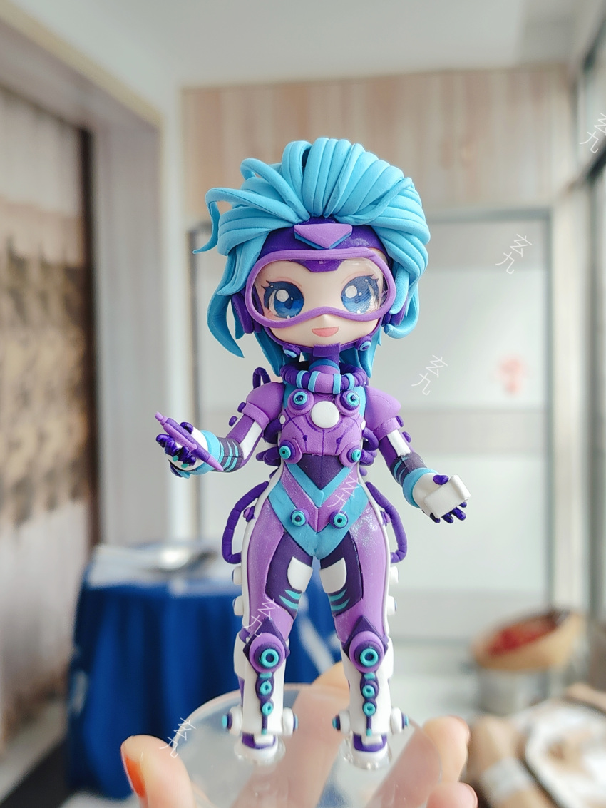 1girl absurdres ai_chi_jianguo_xiaosong_xu animification apex_legends artist's_hand_in_frame blue_bodysuit blue_eyes blue_hair blurry blurry_background bodysuit chinese_commentary clay_(medium) gloves goggles highres holding holding_pen horizon_(apex_legends) looking_at_viewer multicolored_bodysuit multicolored_clothes official_alternate_costume open_mouth overfloater_horizon pen photo_(medium) purple_bodysuit short_hair smile solo unconventional_media white_gloves