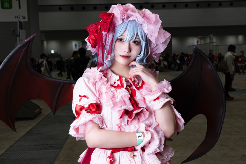 1girl absurdres ascot bat_wings blue_hair bow brooch closed_mouth collared_shirt comiket_103 cosplay cosplay_photo frilled_shirt_collar frills hair_between_eyes hat highres indoors jewelry looking_at_viewer medium_hair mob_cap nocomof photo_(medium) pink_hat pink_shirt red_ascot red_bow red_brooch red_eyes remilia_scarlet shirt sleeve_bow solo_focus touhou wings wrist_cuffs
