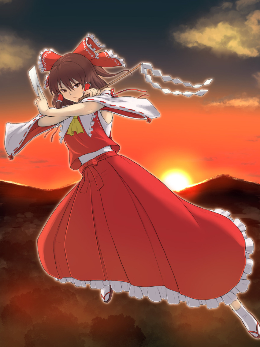 1girl ascot bow brown_eyes brown_hair closed_mouth clouds commentary detached_sleeves frilled_skirt frills full_body gohei gradient_sky hair_bow hair_tubes hakurei_reimu highres holding kakone long_skirt looking_at_viewer ofuda outdoors red_bow red_shirt red_skirt ribbon-trimmed_sleeves ribbon_trim shide shirt sidelocks skirt sky socks solo sun sunset touhou white_socks wide_sleeves yellow_ascot