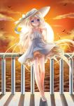  1girl bare_shoulders blonde_hair blue_eyes dress hat highres kokutou_mimi legs long_hair ocean original sky slippers smile solo sunset water 